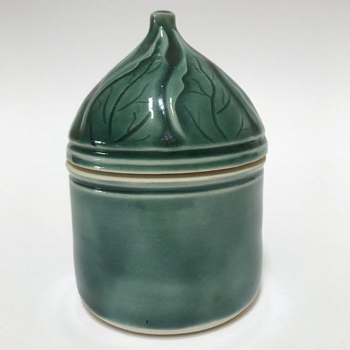 Item 127<br>Porcelain lidded pot with carved leaves on lid in a teal green celadon glaze<br>4.5 in tall x 3.0 in wide<br><b>Sold</b>